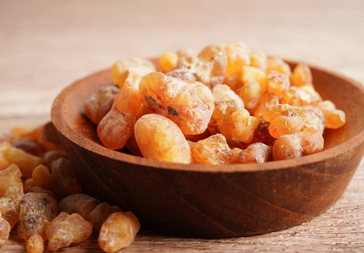A wooden bowl filled with amber-colored frankincense resin pieces, with some resin scattered on a wooden surface nearby.